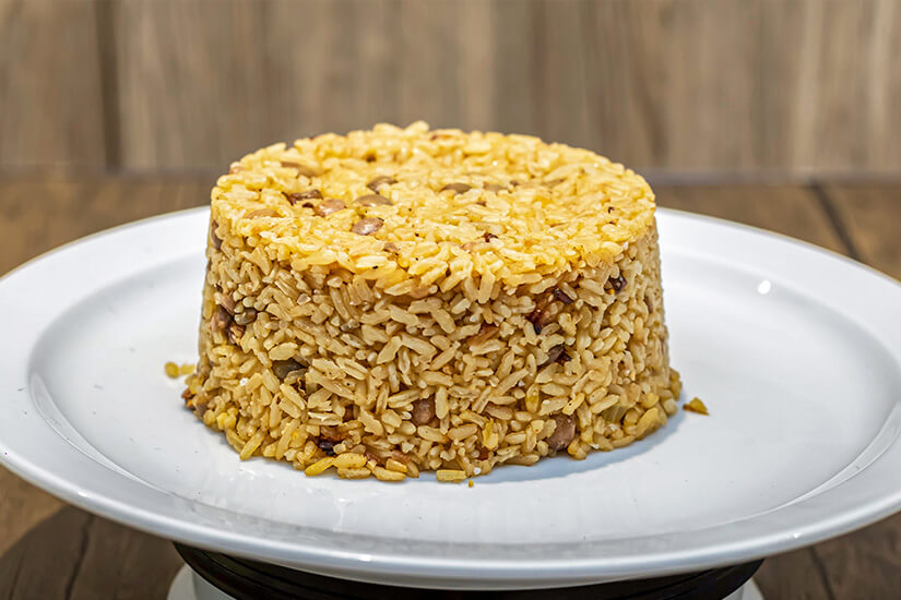 Auf einem weißen Teller thront kuppelförmig geschichteter goldgelber Reis, vermischt mit kleinen bräunlichen Erbsen (Taubenerbsen). Dominikanische Republik Essen Moro de Guandules