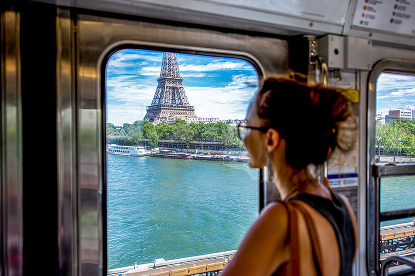 Eine Reisende schaut aus dem Fenster der Pariser Metro auf den Eiffelturm und die Seine. Der Moment fängt genau das ein, was Bahnreisen ausmacht: Ankommen, ohne den Boden schon berührt zu haben. Städtereisen Bahn Paris