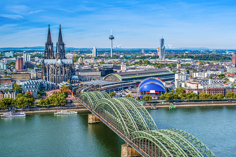 Blick über Köln mit den markanten Doppeltürmen des Doms, der stählernen Hohenzollernbrücke und dem Rhein im Vordergrund. Der Colonius-Fernsehturm und moderne Hochhäuser vervollständigen die charakteristische Silhouette. Städtereisen Bahn Köln