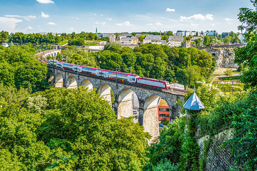 Nahaufnahme des historischen Steinviadukts, über das der luxemburgische Zug rollt. Umgeben von dichtem Grün und alten Festungsmauern wird die Fahrt selbst zum Erlebnis. Städtereisen Bahn Luxemburg