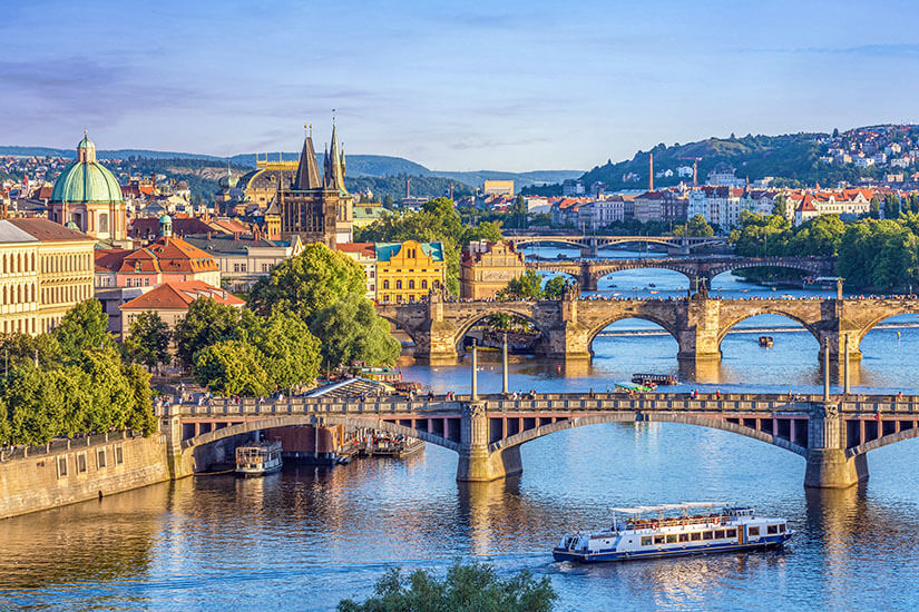 Blick auf die berühmte Karlsbrücke und weitere historische Brücken über die Moldau. Im warmen Abendlicht zeichnen sich die Türme und Kirchtürme der Goldenen Stadt scharf gegen den Himmel ab. Städtereisen Bahn Prag