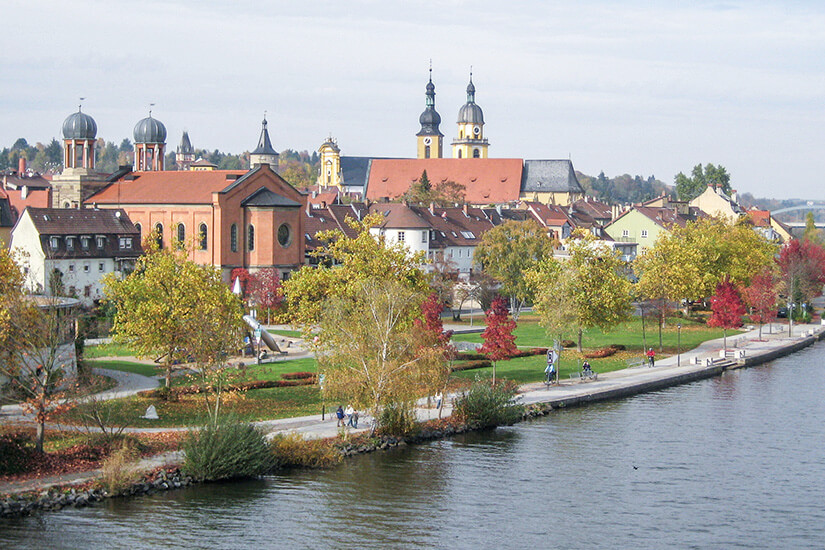 Die Stadt Kitzingen mit Kirchtürmen und idyllischen Häusern sitzt am Ufer des Mains. Herbstlich gefärbte Bäume säumen das Ufer. Kitzingen Unterfranken Willkommen