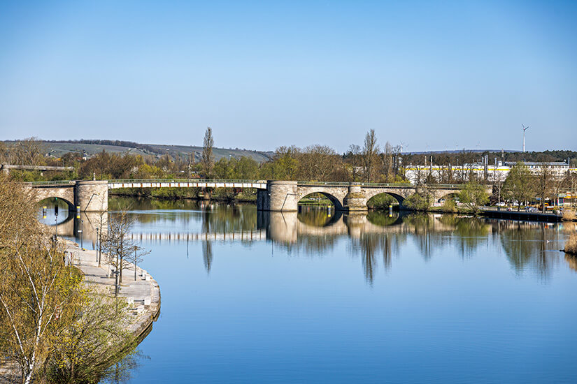 Die Alte Mainbrücke in Kitzingen führt über den Fluss. Ihre steinernen Bogen spiegeln sich im Wasser wider. Kitzingen Unterfranken Mainbruecke