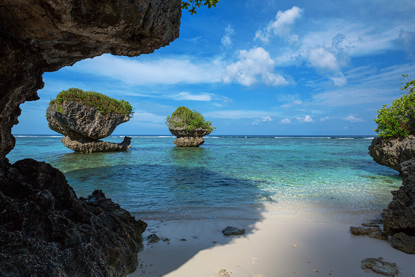 Tanguisson Beach liegt zwischen markanten Kalksteinfelsen, die dem Strand einen geschützten Rahmen geben. Das flache Wasser ist klar, der helle Sand bleibt im Vordergrund angenehm ruhig. Guam Mikronesien Tanguisson Beach
