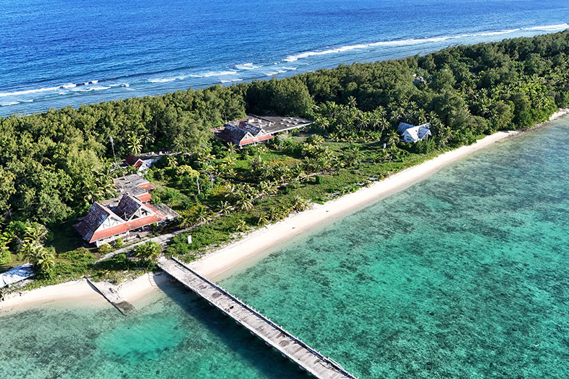 Cocos Island liegt wie ein schmaler grüner Streifen zwischen Lagune und offenem Meer. Der lange Steg führt über seichtes Wasser zur kleinen Insel, deren dichter Bewuchs bis nah an den Strand reicht. Guam Mikronesien Cocos Island