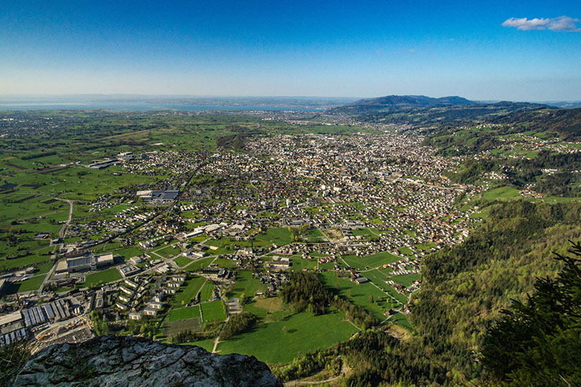 Von einem erhöhten Standort reicht der Blick über Dornbirn, das Rheintal und die umliegenden Hänge. Wohngebiete, Gewerbeflächen und grüne Felder liegen dicht beieinander. Dornbirn Österreich Stadt