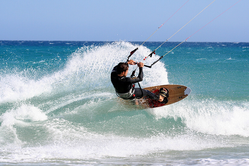 Ein Kitesurfer mit schwarzem Anzug surft über eine Welle im Meer. Kitesurfing Vietnam