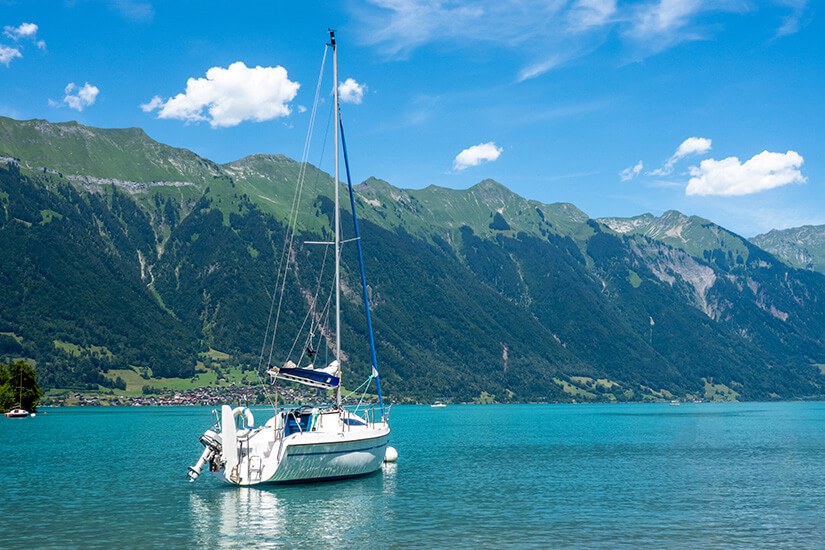 Ein weißes Segelboot schippert über das türkisblaue Wasser des Brienzer Sees. Grüne Berge säumen das Ufer. Brienz Schweiz Segeln