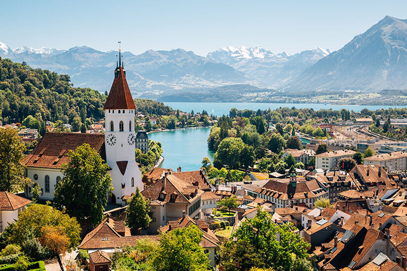 Die Stadt Thun mit Kirchturm und roten Dächern ist zu sehen. Im Hintergrund liegen der See und Berggipfel. Brienz Schweiz Thun