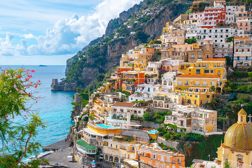 Positano schmiegt sich in all seiner Farbenpracht an den steilen Hang über dem Tyrrhenischen Meer. Orange, Rosa und Terrakotta dominieren die dicht gestaffelten Fassaden, während unten die markante Kuppel der Chiesa Santa Maria Assunta hervorblitzt. Kaum ein Motiv verkörpert die Amalfiküste so perfekt wie dieser Blick auf eines ihrer schönsten Dörfer. Amalfiküste Italien Positano