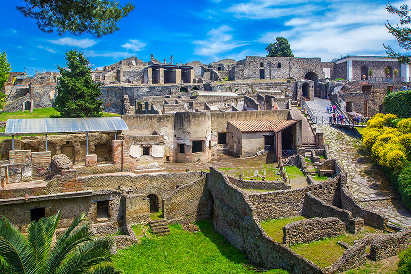 Die Ausgrabungsstätte von Pompeji gibt einen faszinierenden Einblick in das Alltagsleben der antiken Römer. Gut erhaltene Mauern, Straßenzüge und Gebäudereste erstrecken sich unter strahlend blauem Himmel, umrahmt von üppigem Grün. Amalfiküste Italien Pompeji