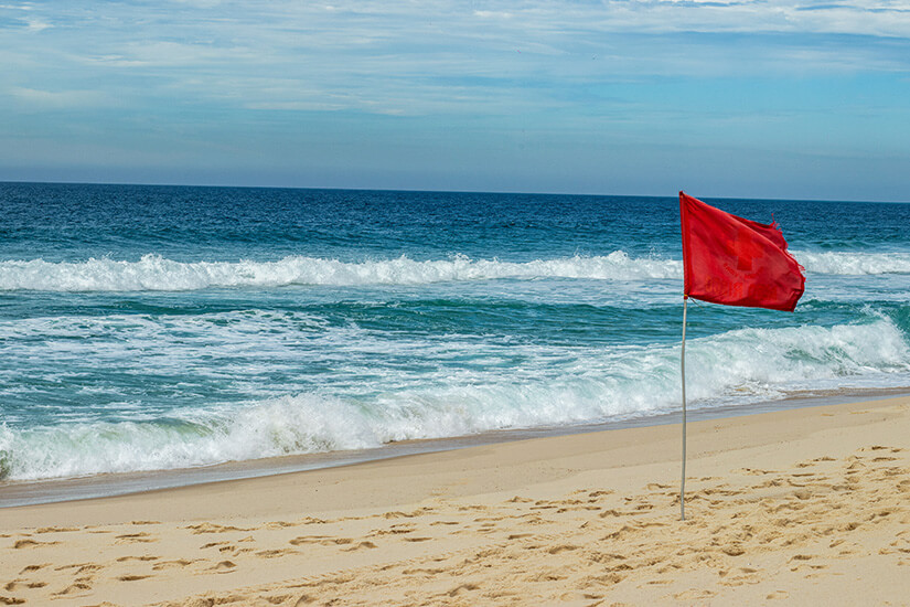 Eine rote Fahne am Meer ist zu sehen. Es herrscht starker Wellengang. Flaggen am Strand rot