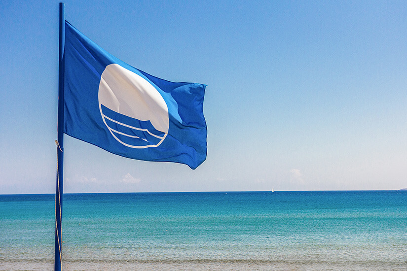 Die Blaue Flagge thront an einem idyllischen Sandstrand mit ruhigem, sauberen Meer. Flaggen am Strand Blau