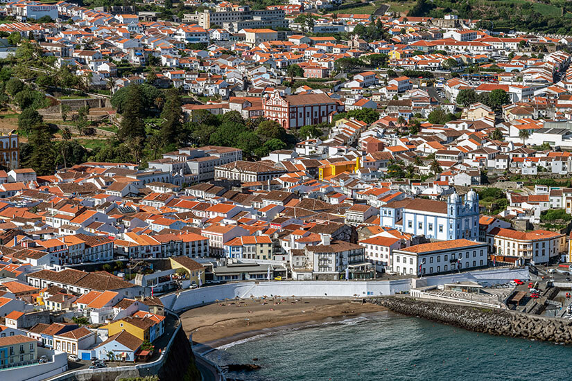 Angra do Heroísmo auf Terceira mit ihren charakteristischen roten Dächern und weißen Fassaden. Die UNESCO-Welterbestadt schmiegt sich malerisch an die Bucht. Geschichte und Atlantik verschmelzen zu einem einzigartigen Stadtbild. Azoren Portugal Heroismo