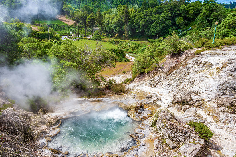 Dampfende Thermalquellen inmitten üppiger Vegetation in Furnas auf São Miguel. Das türkisfarbene Wasser steht im Kontrast zum satten Grün der umliegenden Hügel. Hier brodelt die Erde buchstäblich unter euren Füßen. Azoren Portugal Furnas