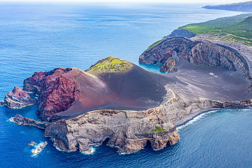 Die Vulkanlandschaft von Capelinhos an der Westspitze Faials aus der Vogelperspektive. Schwarze Asche, rötliches Gestein und das tiefblaue Meer treffen hier aufeinander. Ein Ort, der wirkt, als gehöre er auf einen anderen Planeten. Azoren Portugal Faial