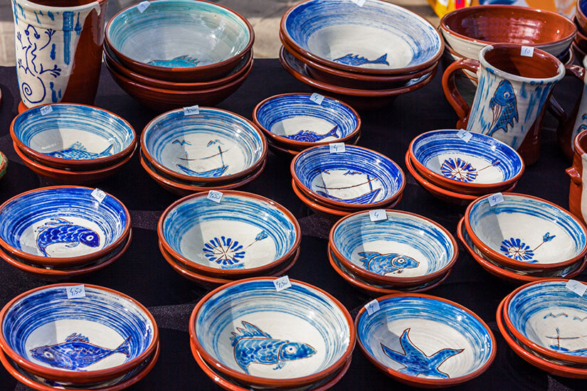 Auf einem dunkel abgedeckten Markttisch stapeln sich zahlreiche handbemalte Keramikschalen aus rötlichem Ton, deren Innenflächen mit blau-weißen Wirbelmustern verziert sind. Mallorca Souvenirs Keramik
