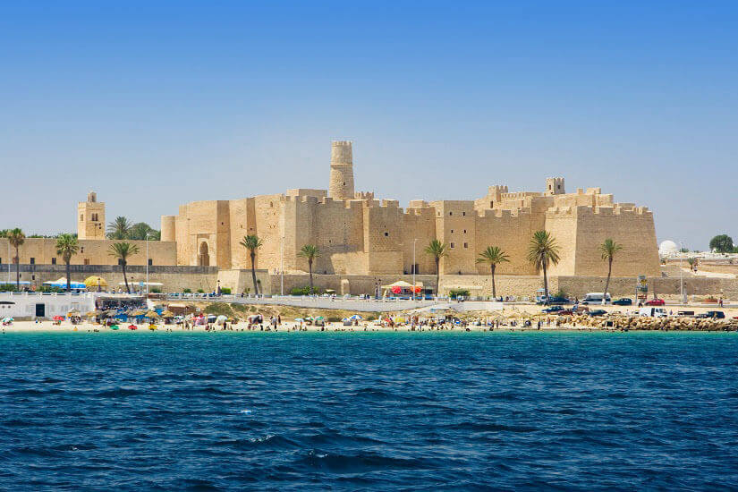 Vom Wasser aus gesehen erhebt sich das wuchtige sandfarbene Ribat von Monastir mit seinen Wehrmauern, Zinnen und dem hohen Wachturm über der Küste. Herbstferien Monastir
