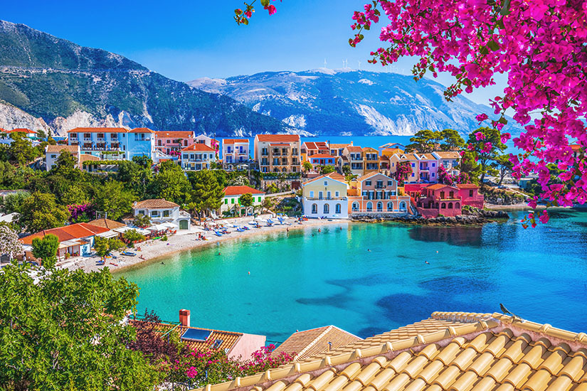 Pastellfarbene Häuser, blühende Bougainvilleen und glasklares Wasser prägen dieses idyllische Küstenmotiv auf Kefalonia. Im Hintergrund steigen bewaldete Berghänge steil empor und geben dem Ort seinen unverwechselbaren ionischen Charakter. Griechsiche Inseln Kefalonia