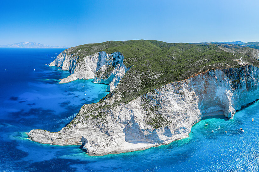 Gewaltige weiße Kalksteinklippen formen an Zakynthos eine dramatische Küstenlinie über dem tiefblauen Ionischen Meer. Kleine Buchten und türkisfarbene Flachwasserbereiche bilden einen starken Kontrast zur rauen Felslandschaft. Griechsiche Inseln Zakynthos