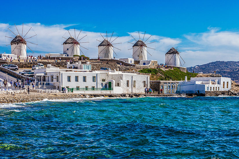 Die berühmten Windmühlen von Mykonos erheben sich über weißen Häusern direkt an der Ägäis. Das Zusammenspiel aus strahlender Architektur, blauem Himmel und bewegtem Meer gehört zu den bekanntesten Motiven der Kykladen. Inseln Mykonos Griechsiche Inseln Mykonos