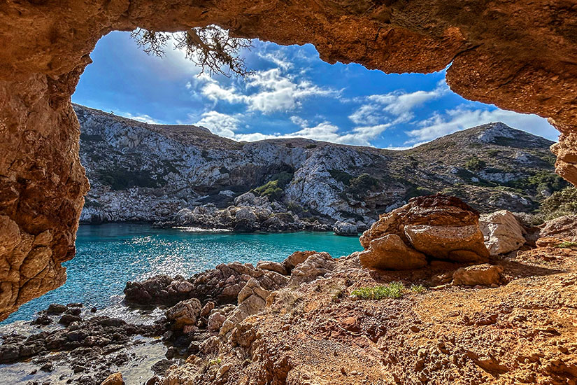 Eine geschützte Bucht auf Ikaria öffnet sich zwischen rauen Felsen zum intensiv türkisfarbenen Meer. Der Blick aus der natürlichen Felshöhle unterstreicht den ursprünglichen Charakter dieser griechischen Insel und vermittelt ein Gefühl von Abgeschiedenheit. Griechsiche Inseln Ikaria