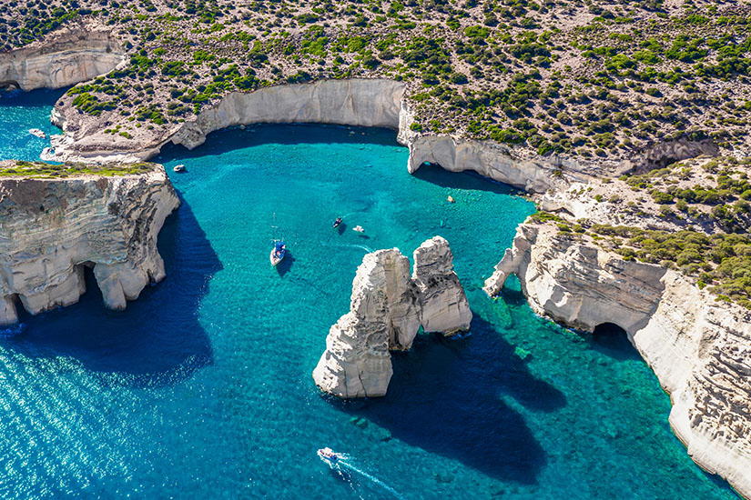 Helle vulkanische Felsformationen rahmen auf Milos eine geschützte Bucht mit kristallklarem Wasser ein. Boote wirken zwischen den bizarren Steinsäulen beinahe winzig und zeigen eindrucksvoll die außergewöhnliche Geologie des Eilands. Griechsiche Inseln Milos