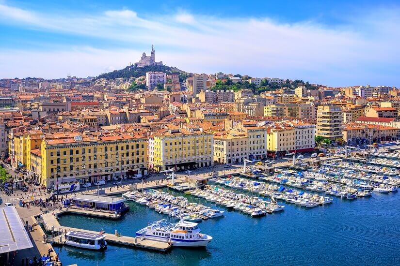 Dicht an dicht liegen weiße Yachten und Ausflugsboote im Alten Hafen von Marseille, gesäumt von einer belebten Kaipromenade mit gelben und ockerfarbenen Häuserfassaden. Herbstferien Marseille