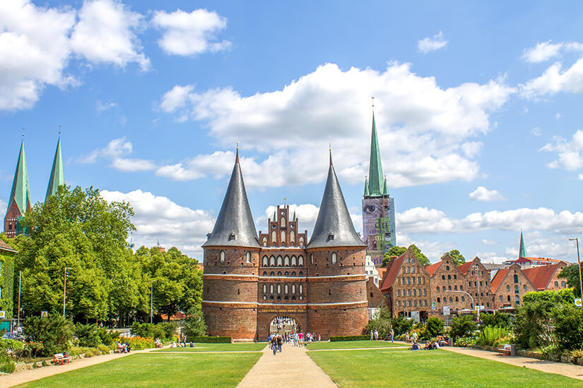 Das Holstentor von Lübeck umgeben von Bäumen, grüner Wiese und anderen Bauwerken. Schoenste Staedte Deutschlands Luebeck