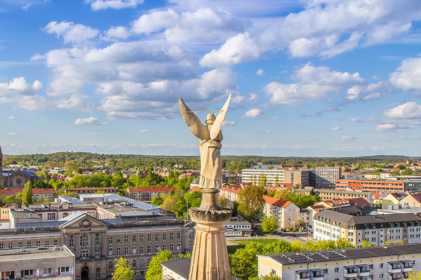 Die Engelsstatue von Potsdam thront über Dächern der Stadt. Im Hintergrund ist grüner Wald zu sehen. Schoenste Staedte Deutschlands Potsdam