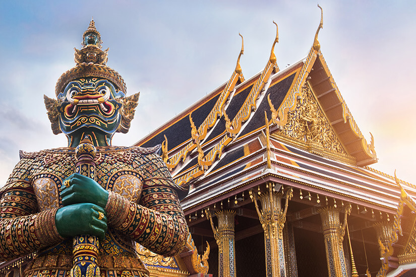Aus der Froschperspektive bewacht ein grüngesichtiger Yaksha-Dämon mit spitzem Helm und mosaikbesetzter Rüstung den Eingangsbereich des Wat Phra Kaeo im Bangkoker Königspalast. Wo ist es im Winter warm Bangkok