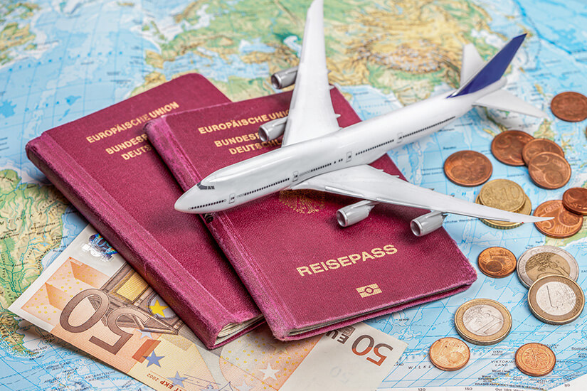 Zu erkennen sind mehrere Reisepässe, ein Modellflugzeug sowie Euro-Scheine und -Münzen auf einer Weltkarte. Die Zusammenstellung symbolisiert Reisen, Reiseplanung und das dafür benötigte Budget. Low Budget Urlaub Einleitung