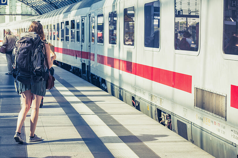 Zu erkennen ist eine Reisende mit großem Rucksack, die auf einem Bahnsteig neben einem Fernzug steht. Die Szene vermittelt den Eindruck einer bevorstehenden Zugreise oder eines Backpacking-Trips. Reisen Spartipps