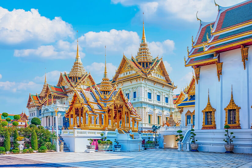 Zu erkennen ist eine prachtvolle Tempel- oder Palastanlage mit reich verzierten, goldenen Dächern und hohen Spitzen. Die farbenfrohe Architektur und die gepflegten Gärten erinnern deutlich an Thailand. Low Budget Urlaub Thailand