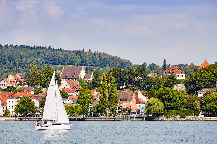 Das Ufer der Stadt Überlingen vom Wasser aus betrachtet. Ein weißes Segelschiff ist zu sehen. Ueberlingen Deutschland Willkommen