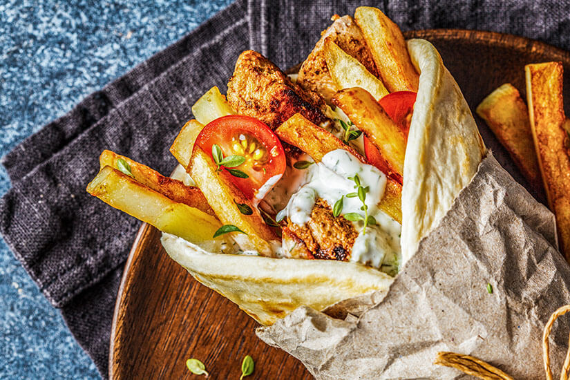 Zu erkennen ist ein gefülltes Fladenbrot mit gegrilltem Fleisch, Pommes frites, Tomaten und einer cremigen Kräutersoße. Zypern Essen Typisch Souvlakia