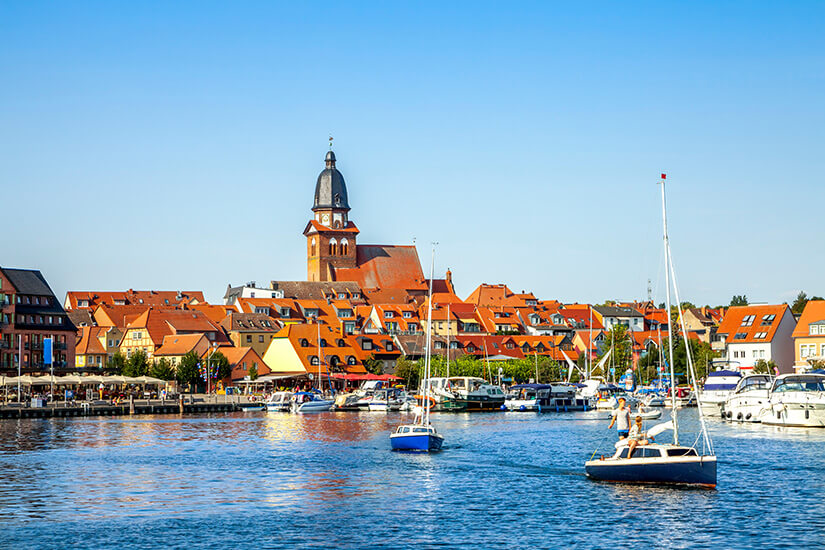 Zu erkennen ist der Hafen von Waren an der Müritz mit zahlreichen Segel- und Motorbooten. Dahinter erstreckt sich die Altstadt mit roten Ziegeldächern und einem markanten Kirchturm. Mecklenburger Seenland Waren