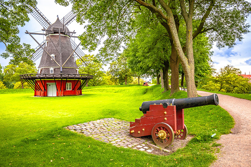 Eine Mühle und eine Kanone sind zwischen Grünanlagen zu sehen. Kopenhagen Sehenswuerdigkeiten Kastellet