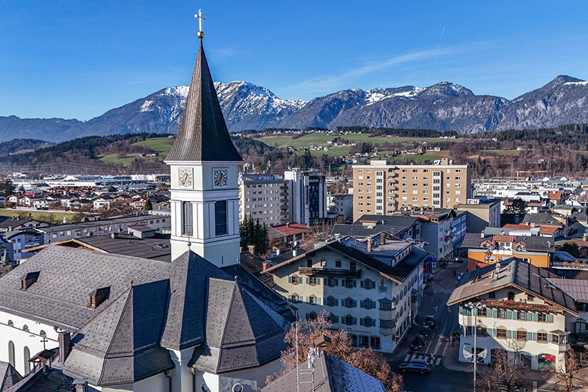 Die Pfarrkirche von Wörgl mit ihrem markanten Turm überragt die Dächer des lebhaften Stadtzentrums. Dahinter erstrecken sich die schneebedeckten Gipfel der umliegenden Alpen und verleihen dem Ortsbild seinen unverwechselbaren Charme. Wörgl Österreich Stadt
