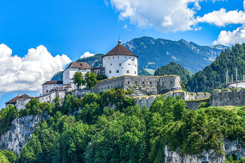 Die imposante Festung Kufstein thront majestätisch auf einem bewaldeten Felsvorsprung über dem Inntal. Mit ihren mächtigen weißen Mauern und dem markanten Kaiserturm zählt die mittelalterliche Anlage zu den bekanntesten Sehenswürdigkeiten in Tirol. Im Hintergrund erstreckt sich die beeindruckende Alpenkulisse bei strahlend blauem Himmel. Wörgl Österreich Festung
