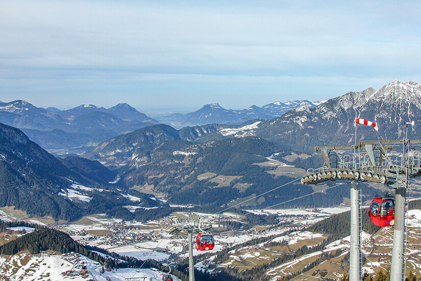 Rote Gondeln schweben über eine verschneite Winterlandschaft mit Blick auf das tief eingeschnittene Inntal und die umliegenden Gipfel. Das Skigebiet nahe Wörgl gehört zu den größten und modernsten Schneerevieren in ganz Österreich. Wörgl Österreich Skipiste