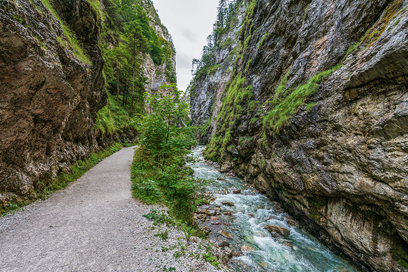 Ein schmaler Wanderweg schlängelt sich durch die eindrucksvolle Kundler Klamm, deren moosbewachsene Felswände steil in die Höhe ragen. Direkt daneben rauscht ein türkisfarbener Wildbach über glattgeschliffene Steine. Wörgl Österreich Kundler Klamm