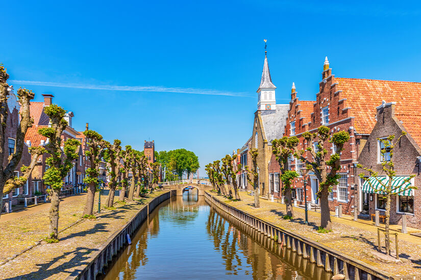 Ein Kanal führt durch die kleine Stadt Sloten, vorbei an Häusern und Bäumen. Lemmer Niederlande Sloten
