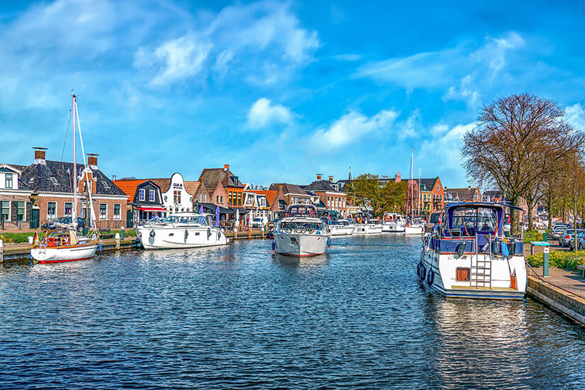Ein Wasserkanal führt durch Lemmer. Weiße Boote treiben darauf, das ufer ist von Häusern gesäumt. Lemmer Niederlande Anreise