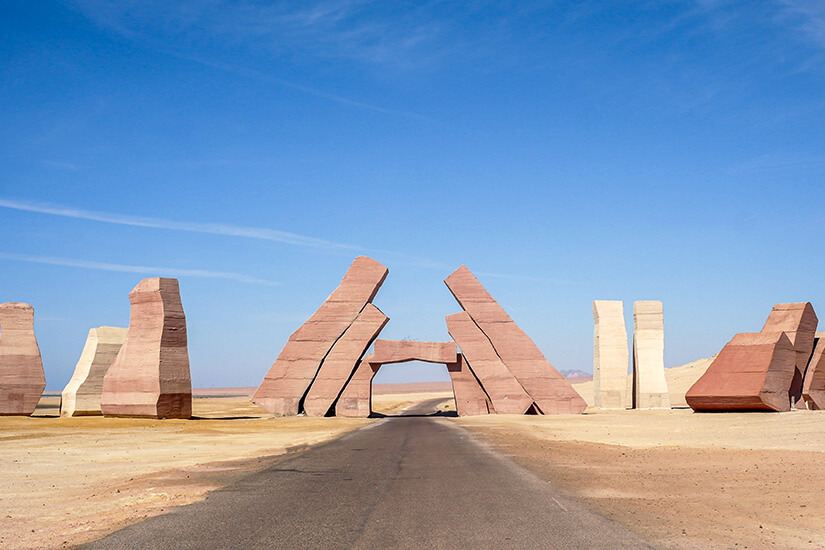 Die markante Eingangskulptur des Nationalparks Ras Mohammed auf der Sinai-Halbinsel, flankiert von monumentalen Sandsteinfiguren. Die schnurgerade Wüstenstraße führt direkt in eines der beeindruckendsten Schutzgebiete des Landes. Ägypten Strände Ras Mohamed