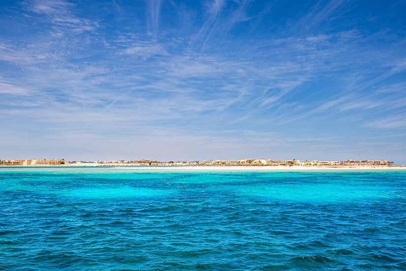 Blick über das leuchtend türkisfarbene Wasser der Soma Bay südlich von Hurghada. Am Horizont zeichnet sich die elegante Silhouette der Resortanlage auf der Halbinsel ab. Soma Bay vereint exklusiven Strandkomfort mit einem der besten Hausriffe am gesamten Roten Meer. Ägypten Strände Soma Bay
