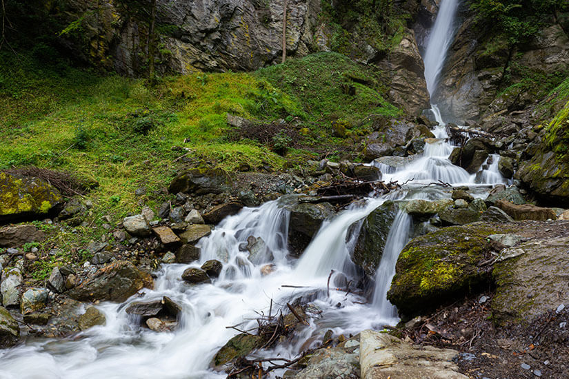 In mehreren Stufen stürzt ein Wasserfall über moosbewachsene Felsblöcke und Geröll zu Tal, durch die lange Belichtung wirkt das Wasser seidig weich. Bischofshofen Gainfeldwasserfall
