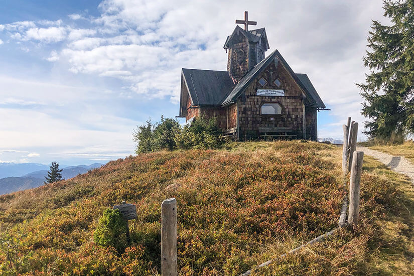 Auf einer herbstlich braun-rot gefärbten Bergkuppe steht eine kleine, mit Holzschindeln verkleidete Kapelle samt Glockenturm und Kreuz. Bischofshofen Hochgruendeck