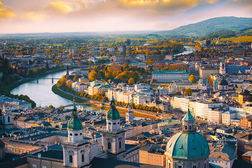 Von oben blickt man über die Altstadt Salzburgs, wo im Vordergrund die grün patinierten Kuppeln und Türme des Doms aufragen und sich dahinter dicht gedrängte Dächer erstrecken. Oesterreich Salzburg