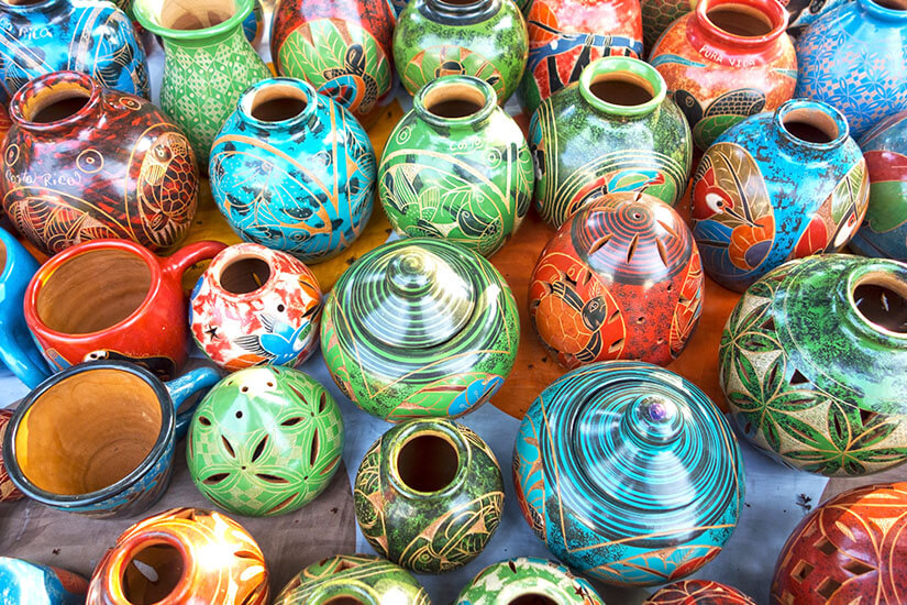 Zu erkennen sind zahlreiche farbenfrohe, handbemalte Keramikgefäße in unterschiedlichen Formen und Größen. Die kunstvollen Muster zeigen vor allem Tiere, Pflanzen und geometrische Ornamente in kräftigen Farben. Costa Rica Andenken Keramik